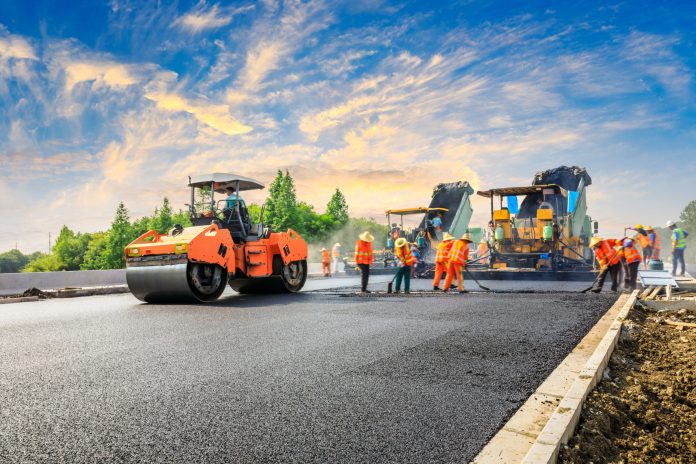 Construction site is laying new asphalt road pavement,road construction workers and road construction machinery scene.highway construction site landscape.